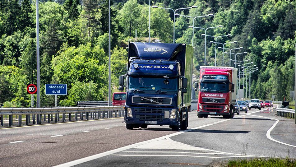 En blå lastebil kjører foran en rød lastebil på motorvei