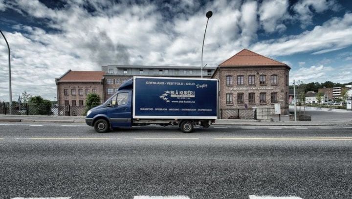 Blå lastebil parkert foran bygning på dagtid