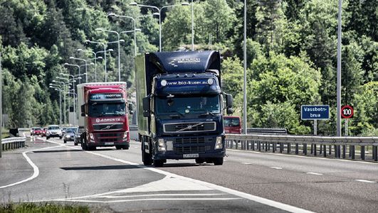 Blå lastebil på vei med skog i bakgrunn